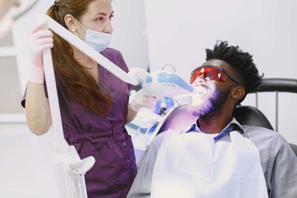 Dentist performing teeth whitening procedure on patient with specialized equipment.