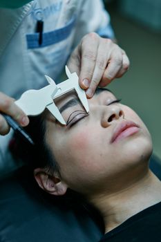 A surgeon measures a patient's eyelid for blepharoplasty preparations.